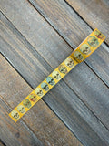 The Bone Parade Washi Tape — unrolled roll of golden-orange washi tape with a repeating weathered skull motif, laid diagonally across a weathered wood surface
