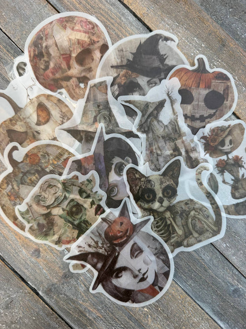 Vellum After Dark Paper Bites — pile of translucent vellum die cuts showing skulls, witches, jack-o-lanterns, a skeleton cat and ghostly faces on a weathered wood surface